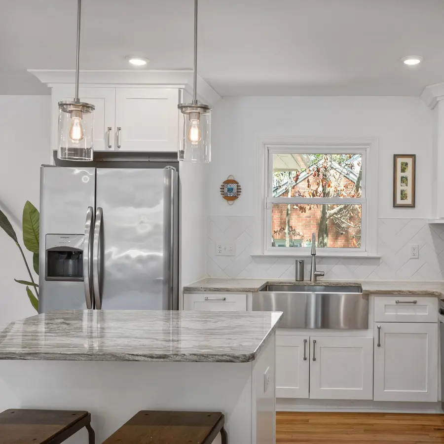 White kitchen with marble countertops, a farmhouse sink and pendant lights