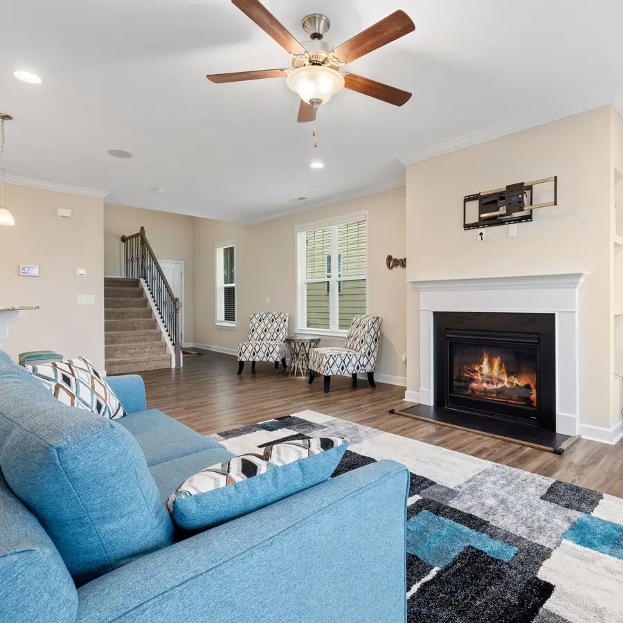 Open living room with crown molding, a fireplace with white mantel and hardwood floors